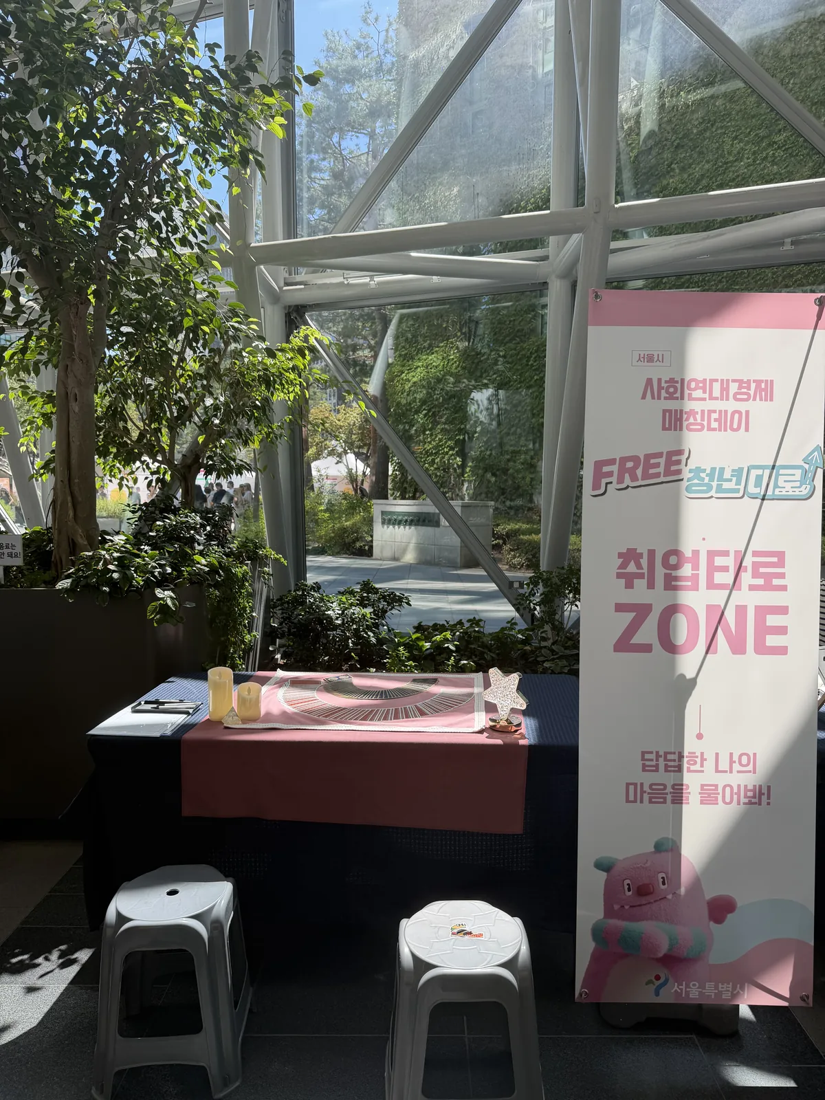 분홍 배너 「취업타로 ZONE」 곁에 차려진 타로 테이블 — 네이비 테이블보 위 분홍 러너와 매트, 그 앞에 놓인 흰 스툴
